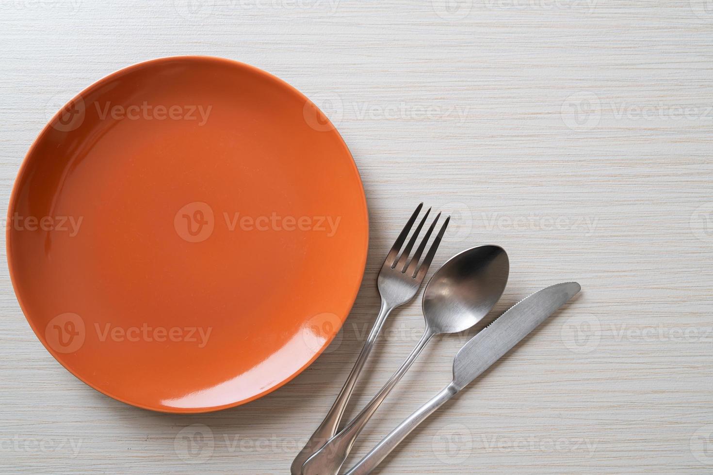Empty plate or dish with knife, fork, and spoon on wood tile background photo