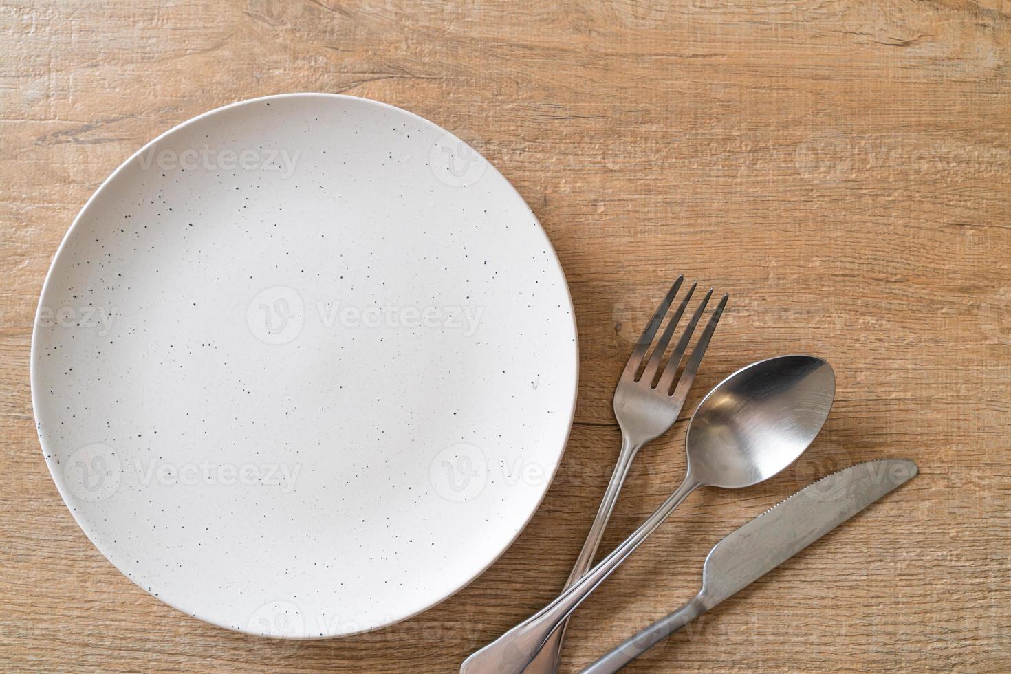 Empty plate or dish with knife, fork, and spoon on wood tile background photo