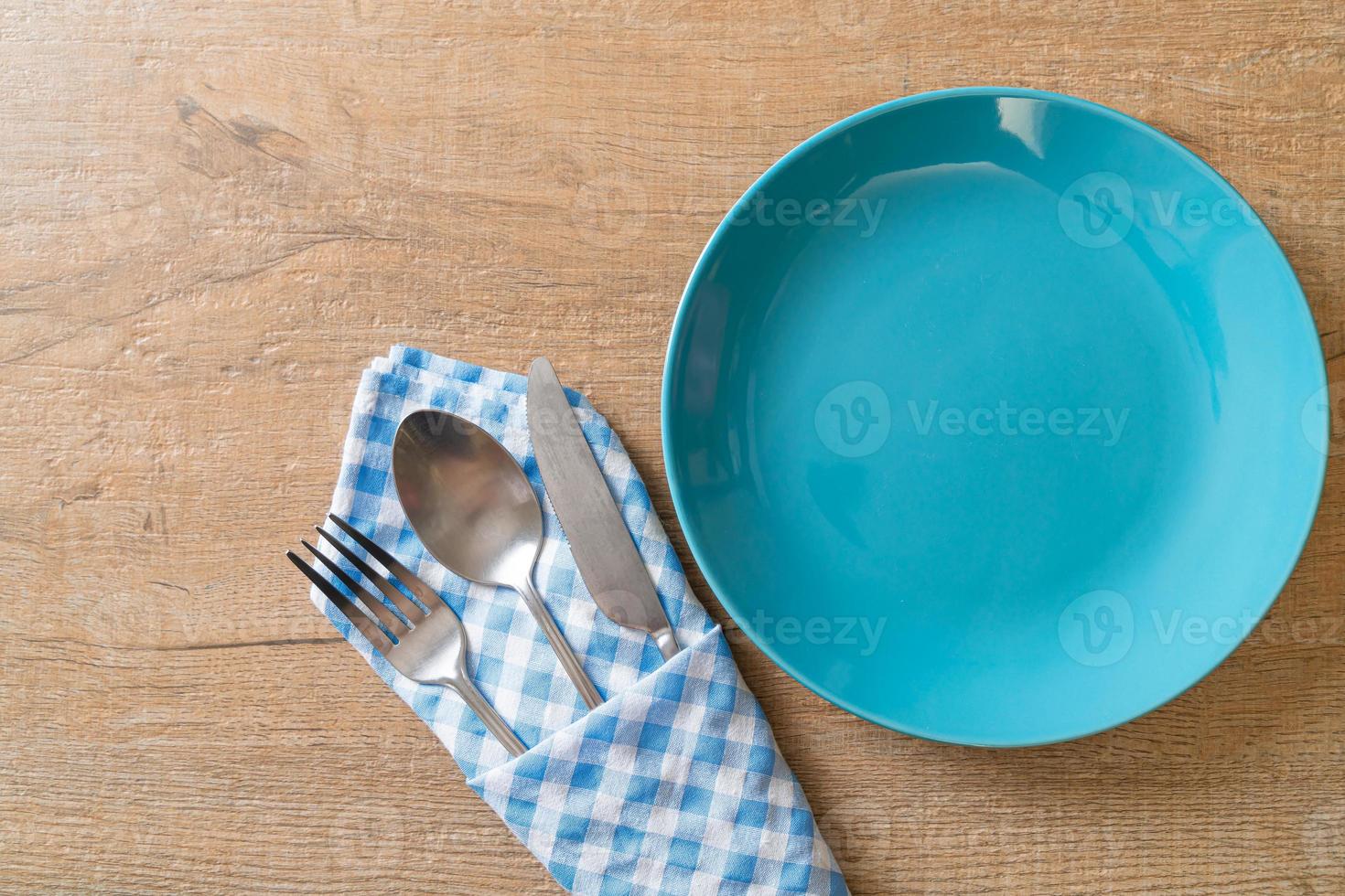 Empty plate or dish with knife, fork, and spoon on wood tile background photo