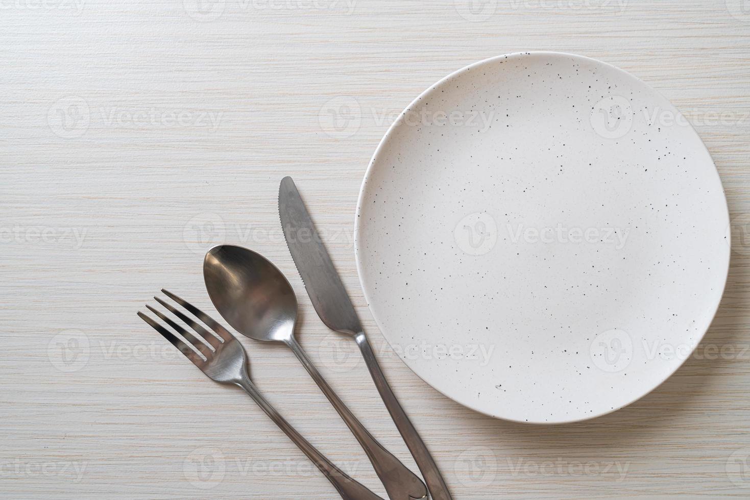 Empty plate or dish with knife, fork, and spoon on wood tile background photo