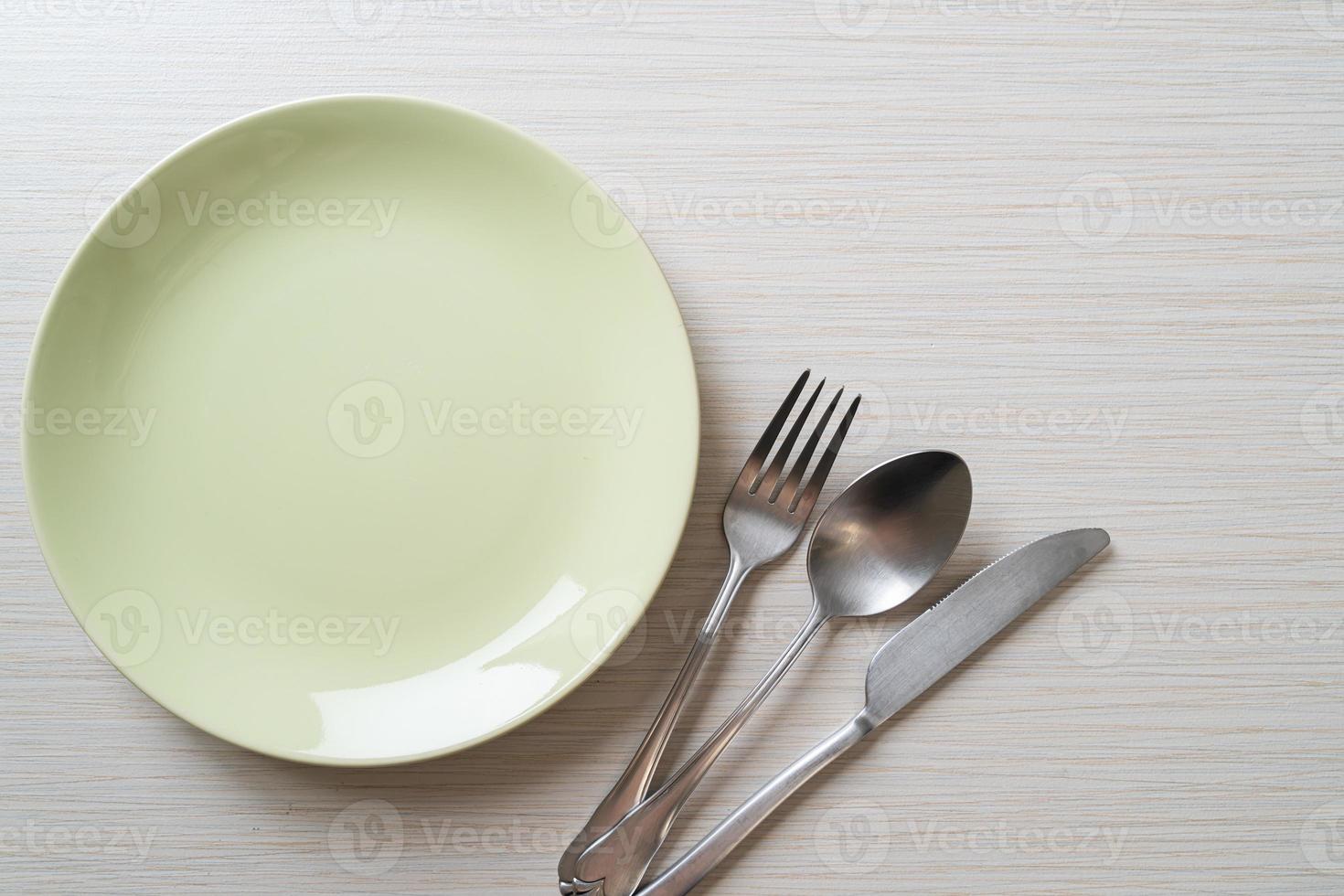 Empty plate or dish with knife, fork, and spoon on wood tile background photo