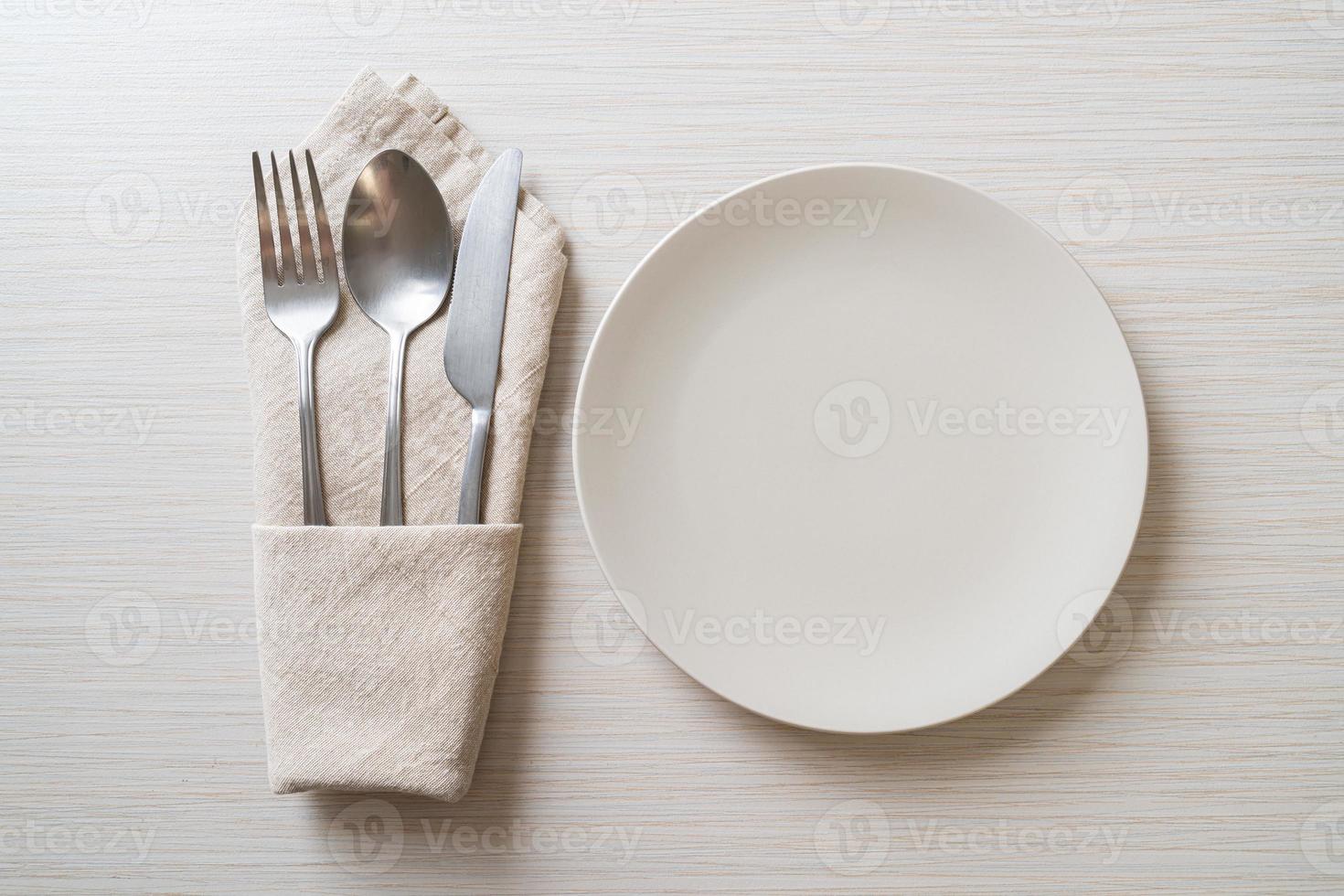 Empty plate or dish with knife, fork, and spoon on wood tile background photo