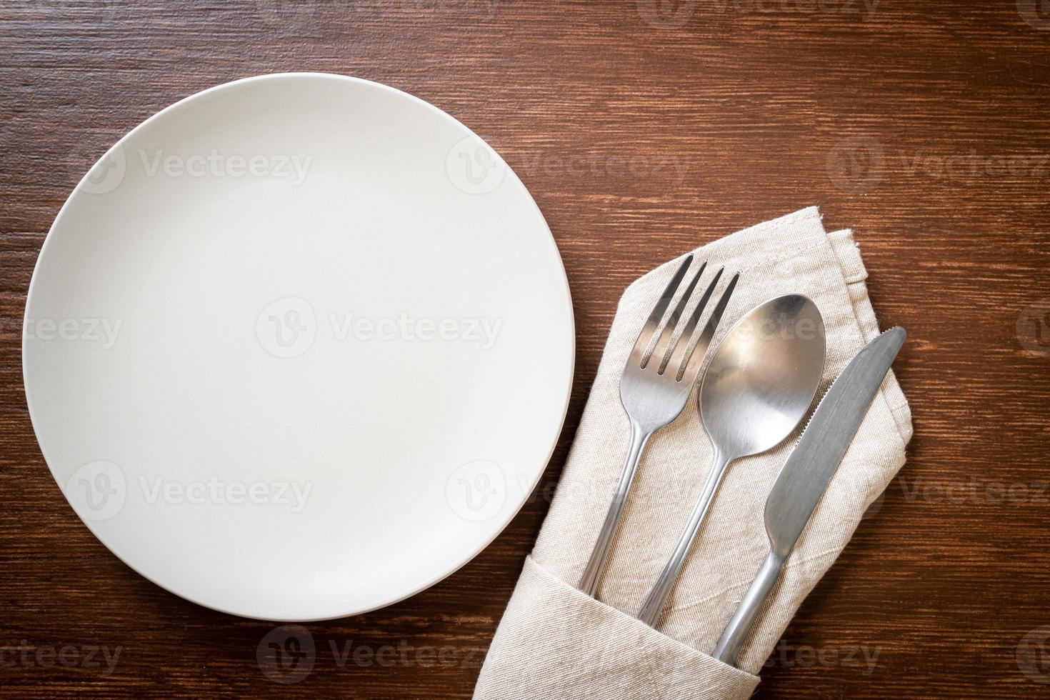 Empty plate or dish with knife, fork, and spoon on wood tile background photo