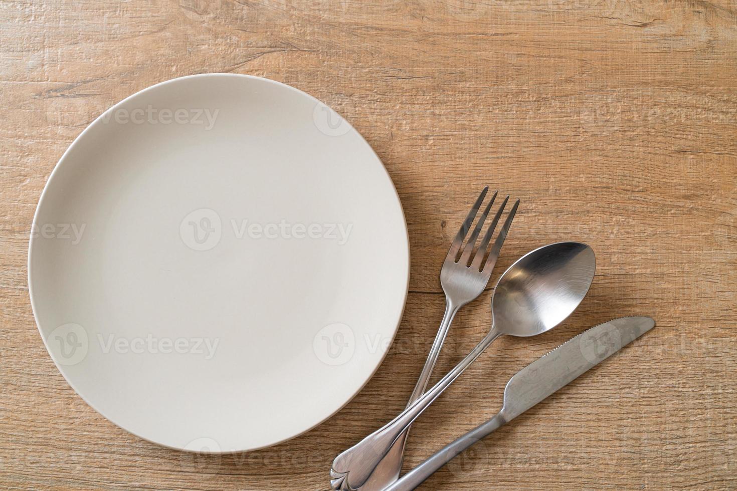 Empty plate or dish with knife, fork, and spoon on wood tile background photo