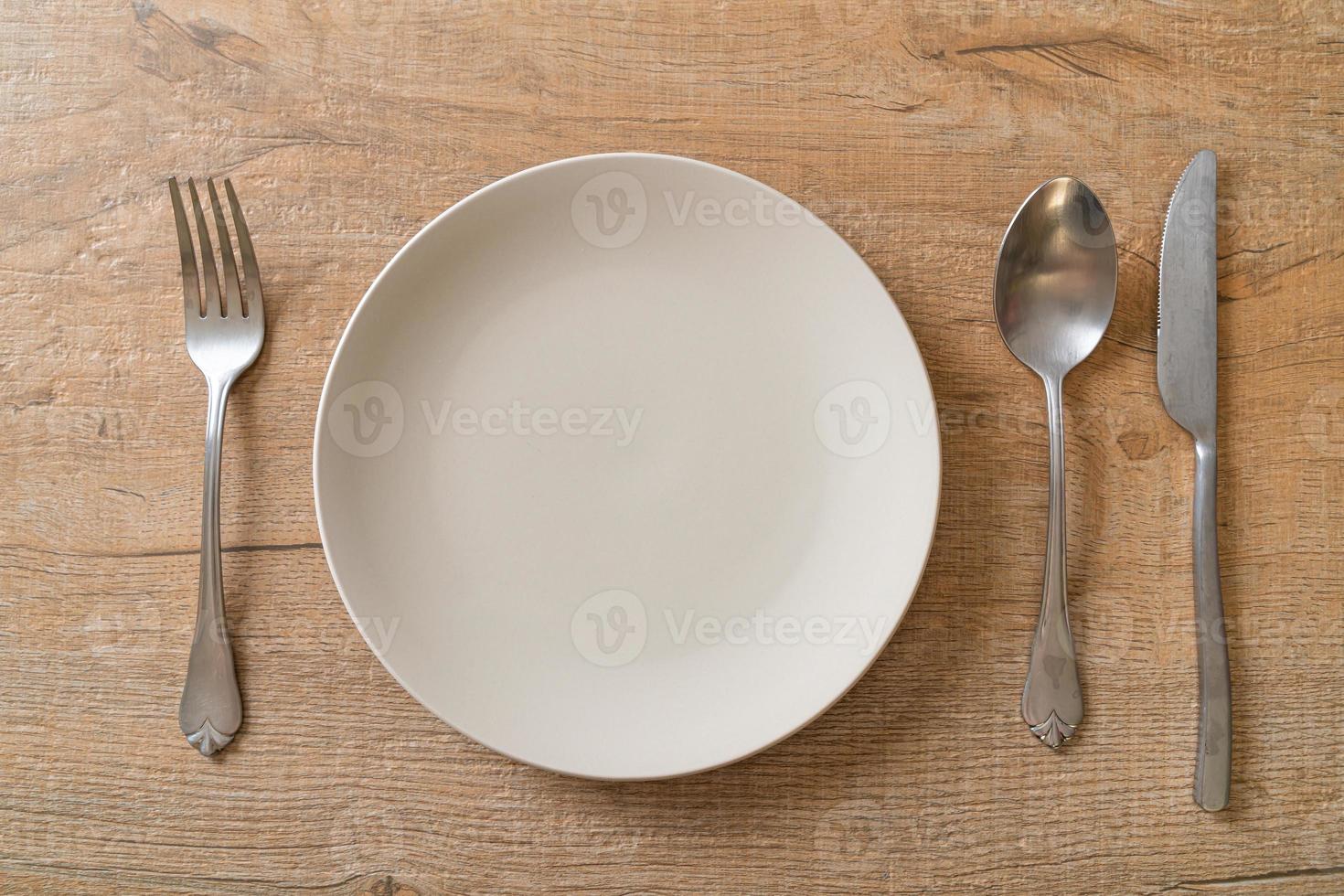 Empty plate or dish with knife, fork, and spoon on wood tile background photo