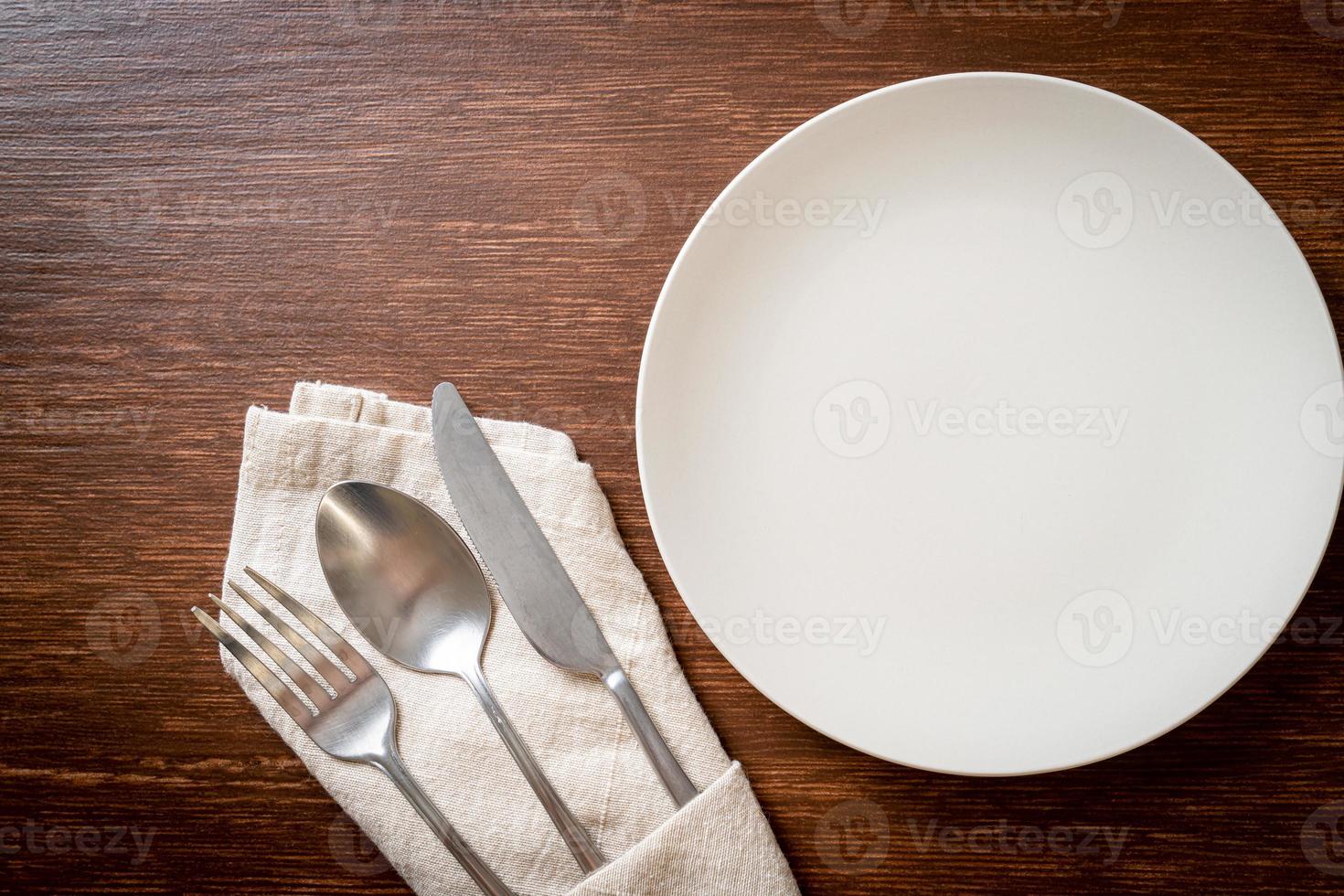 Empty plate or dish with knife, fork, and spoon on wood tile background photo