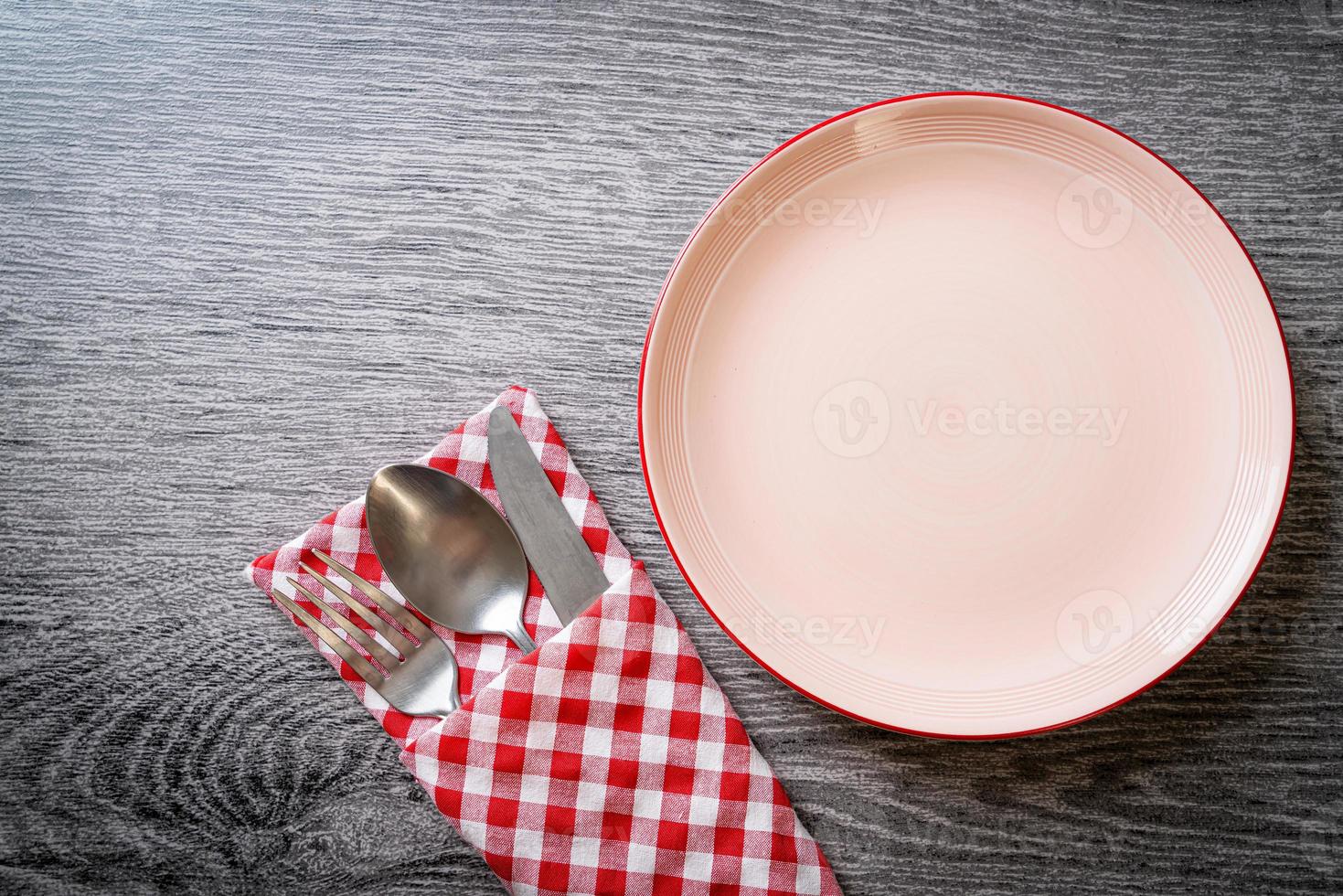 Empty plate or dish with knife, fork, and spoon on wood tile background photo