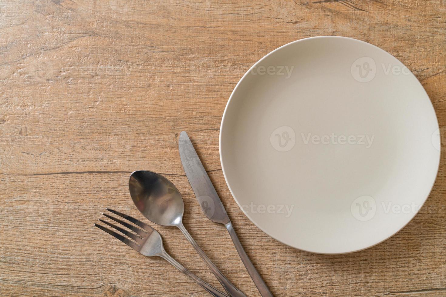 Empty plate or dish with knife, fork, and spoon on wood tile background photo