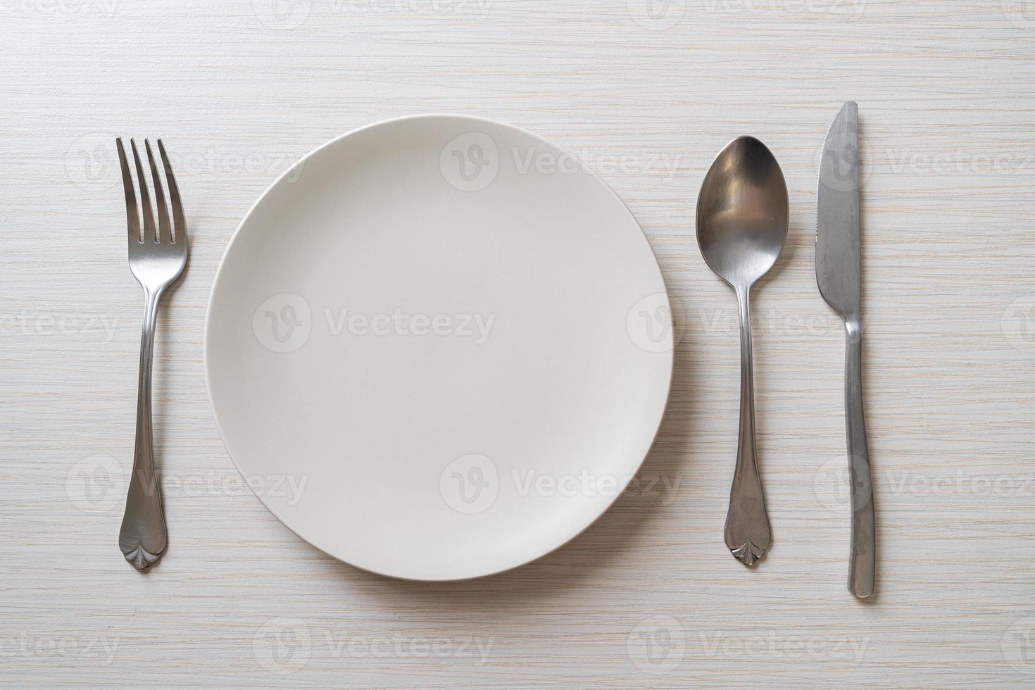 Empty plate or dish with knife, fork, and spoon on wood tile background photo