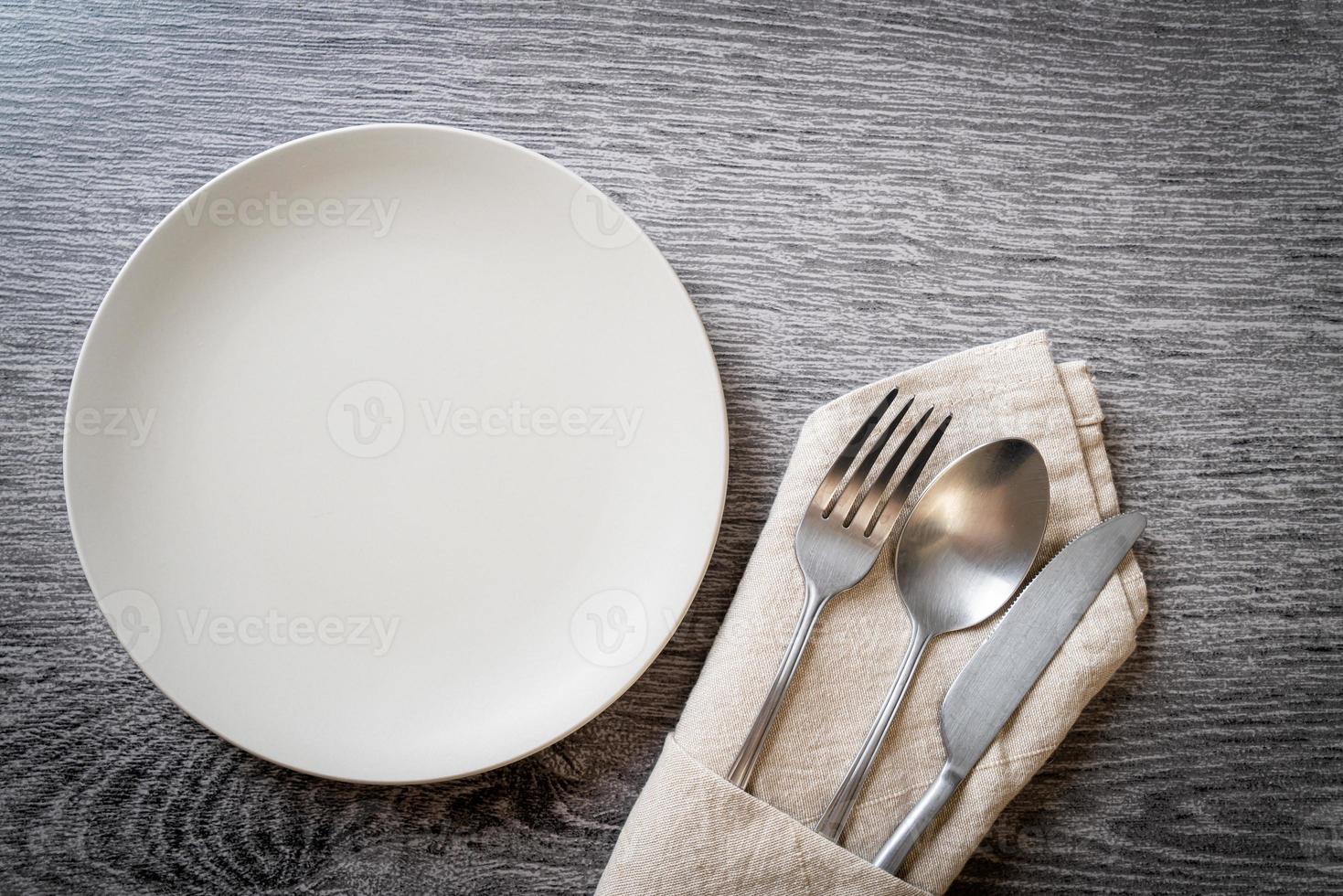 Empty plate or dish with knife, fork, and spoon on wood tile background photo