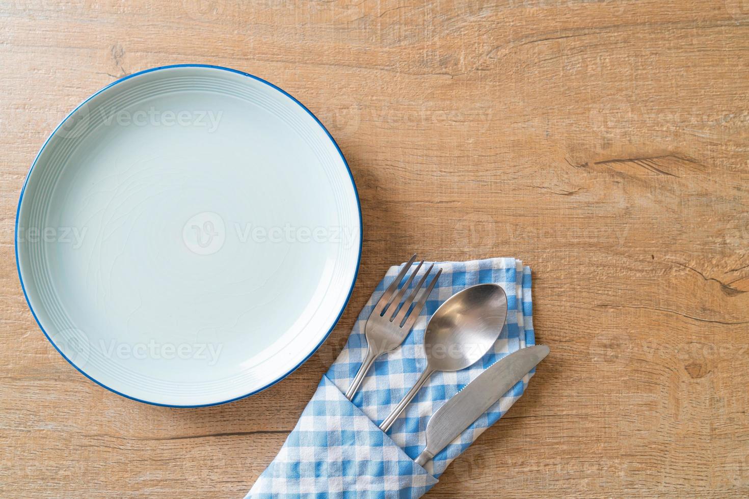 Empty plate or dish with knife, fork, and spoon on wood tile background photo