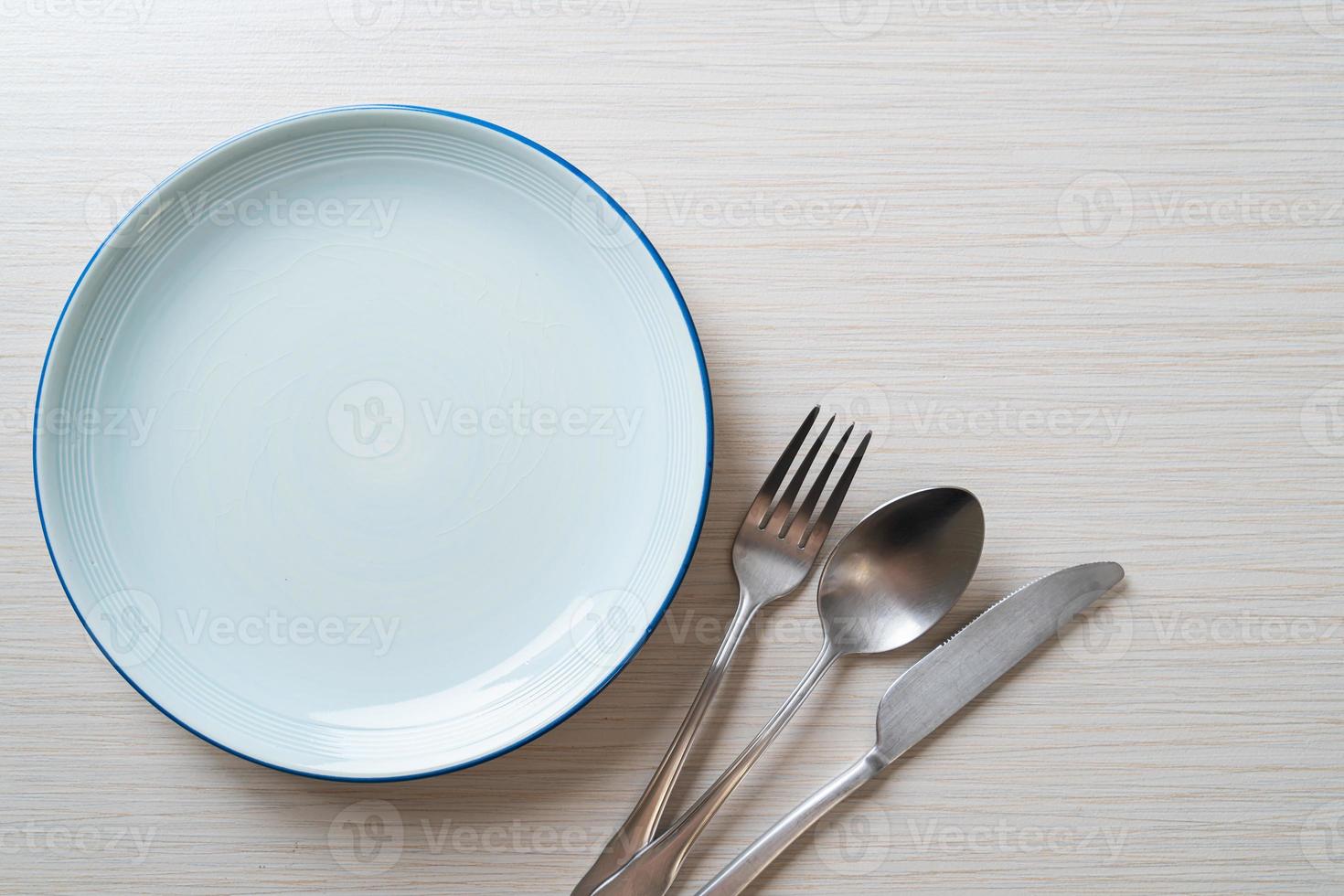 Empty plate or dish with knife, fork, and spoon on wood tile background photo