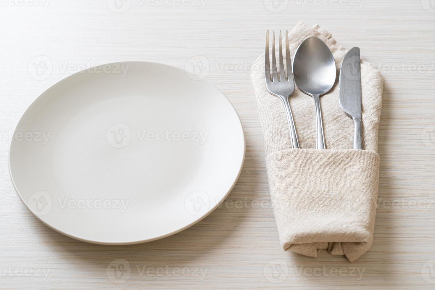 Empty plate or dish with knife, fork, and spoon on wood tile background photo