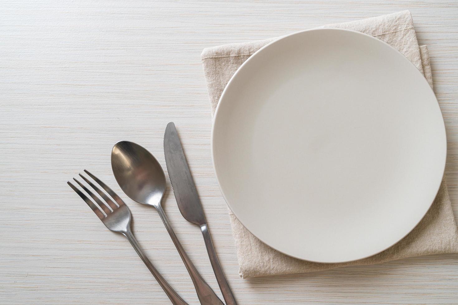 Empty plate or dish with knife, fork, and spoon on wood tile background photo