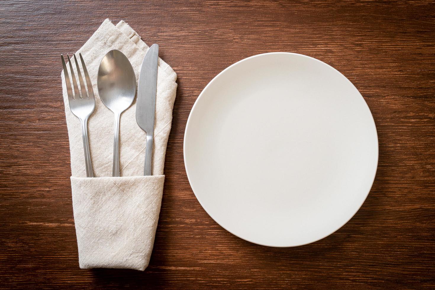 Empty plate or dish with knife, fork, and spoon on wood tile background photo