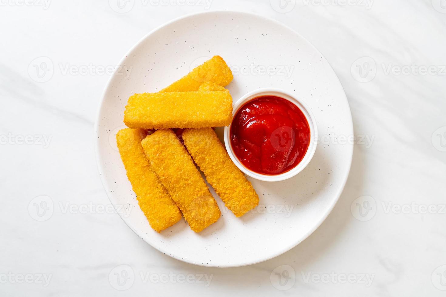 Palitos de pescado frito crujiente con pan rallado servido en un plato con salsa de tomate foto