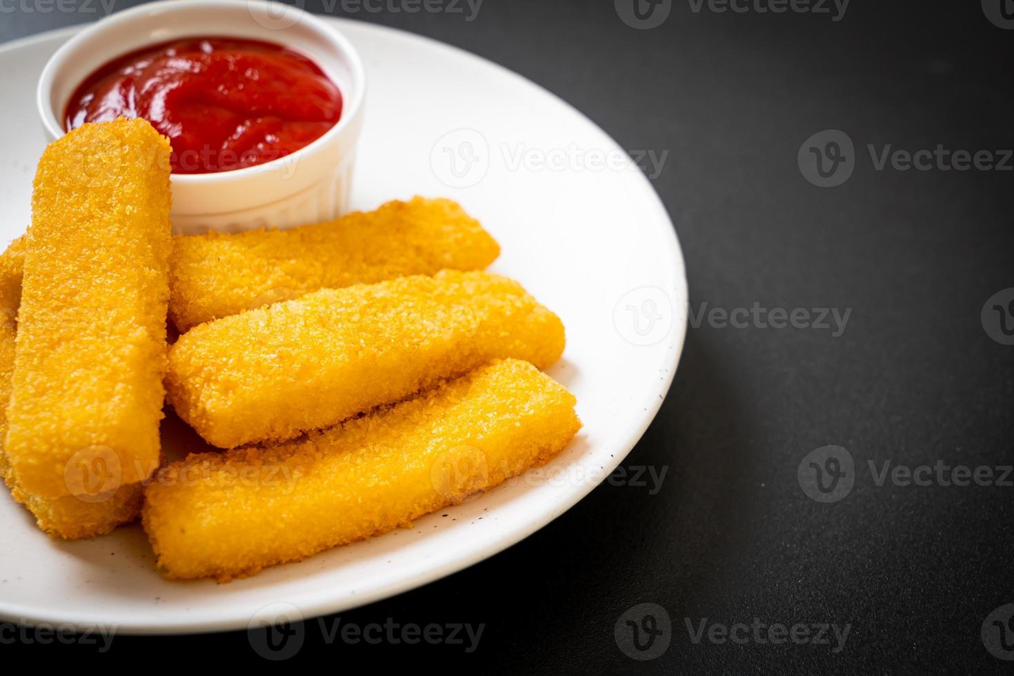 Palitos de pescado frito crujiente con pan rallado servido en un plato con salsa de tomate foto