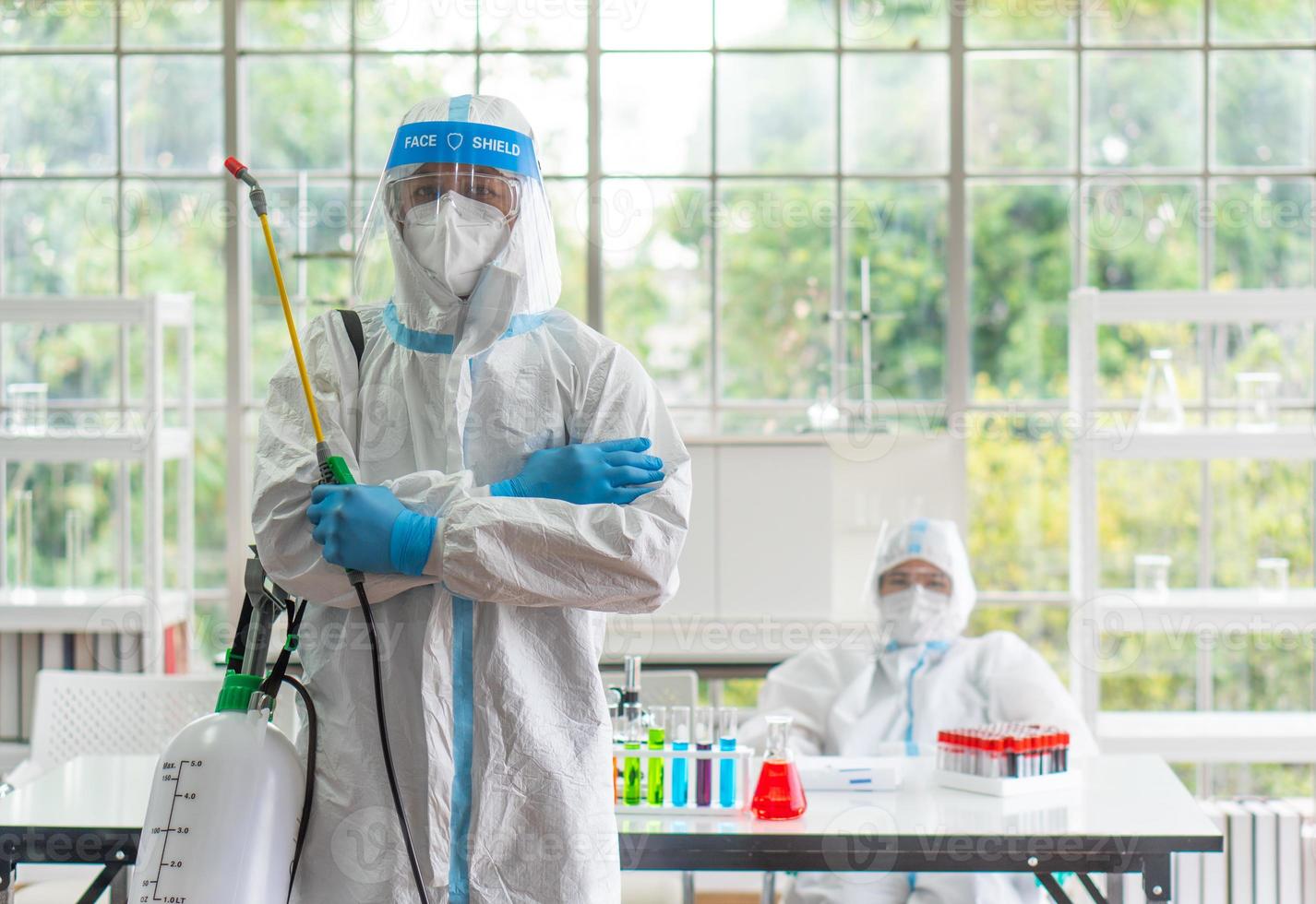 Worker from decontamination services wearing personal protective equipment or ppe including suit, face shield and mask. He uses disinfectant to spray and clean scientist lab photo