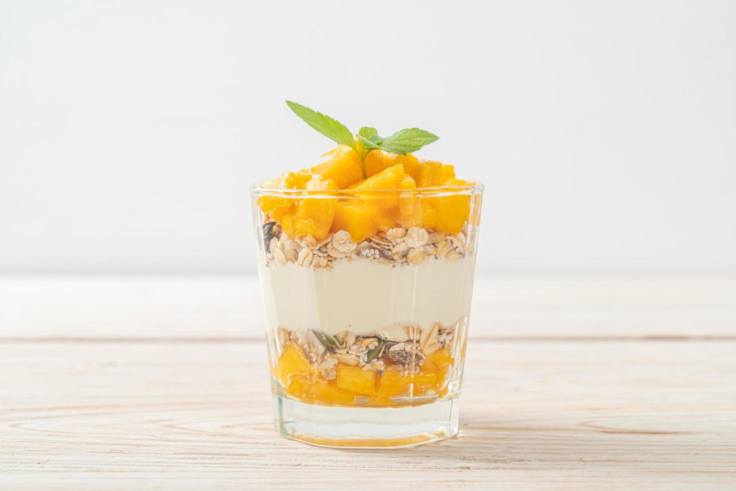 Yogur de mango fresco con granola en vidrio - estilo de comida saludable foto