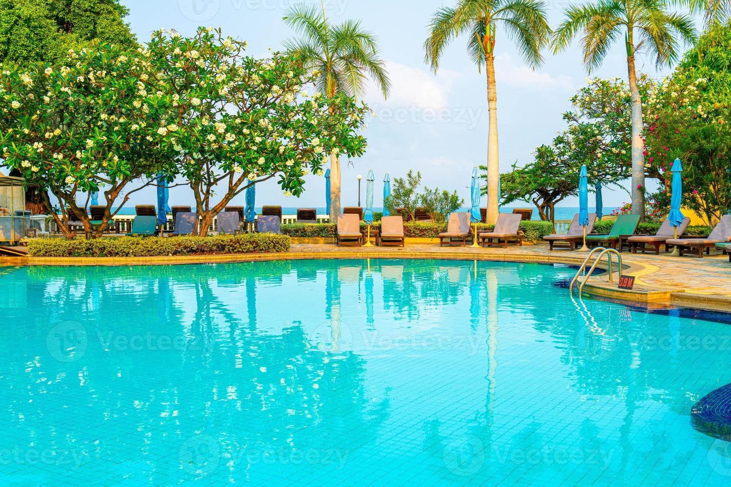sillas de piscina y sombrillas alrededor de la piscina con cocoteros - vacaciones y concepto de vacaciones foto