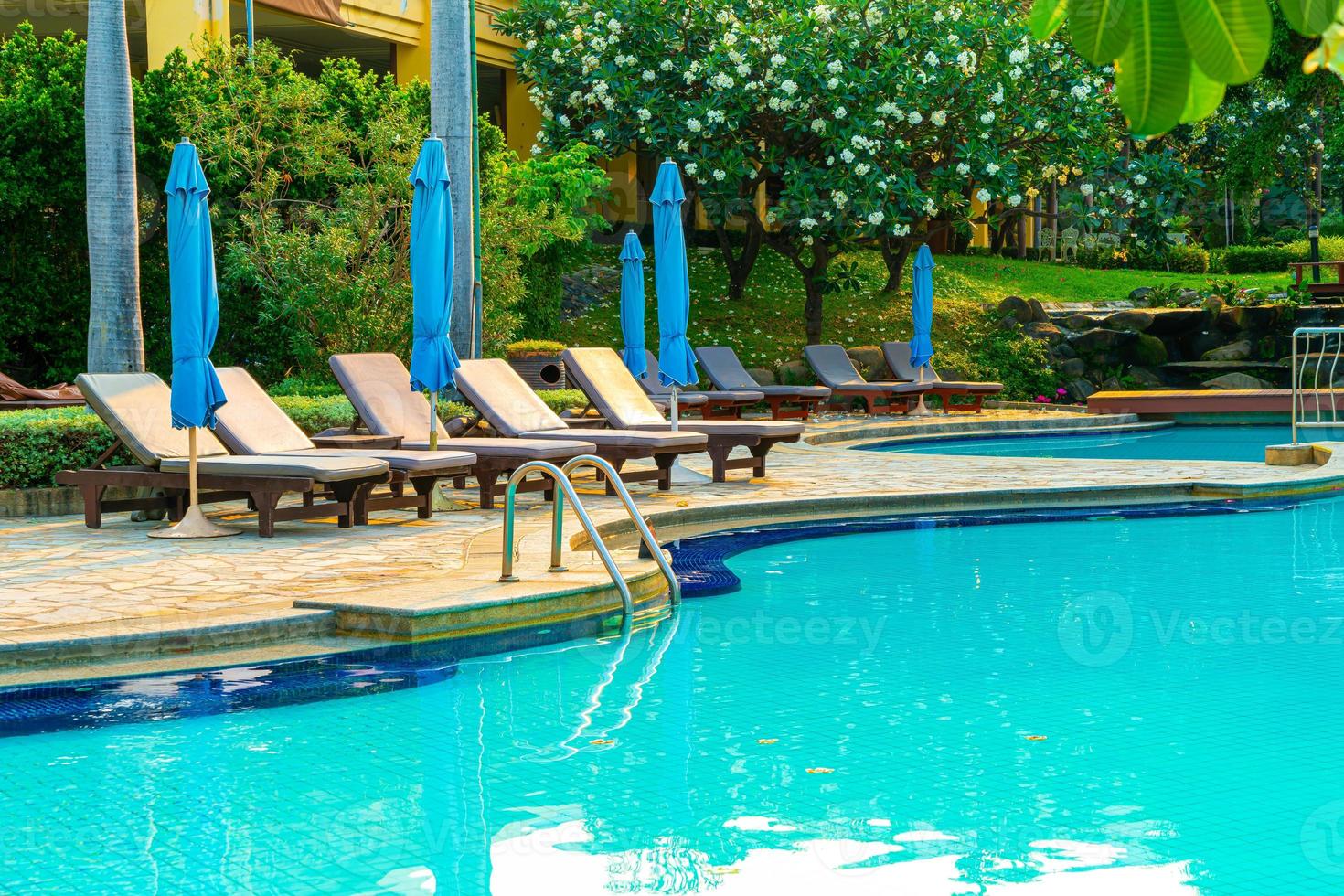 Chair pools and umbrellas around swimming pool with coconut palm trees - Holidays and vacation concept photo