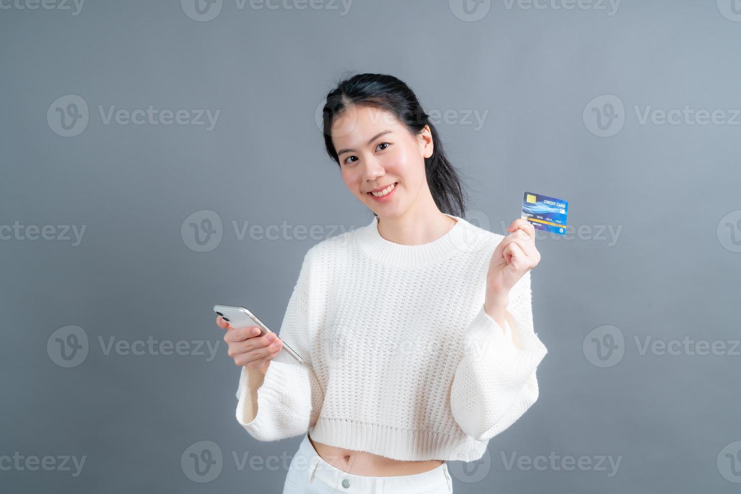 Young Asian girl showing plastic credit card while holding mobile phone photo