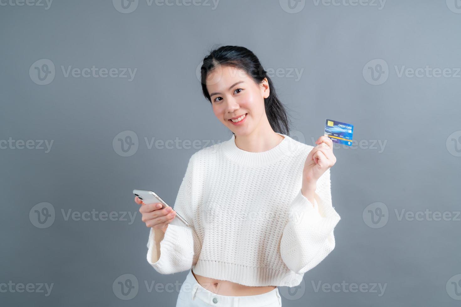 Joven asiática mostrando una tarjeta de crédito de plástico mientras sostiene el teléfono móvil foto