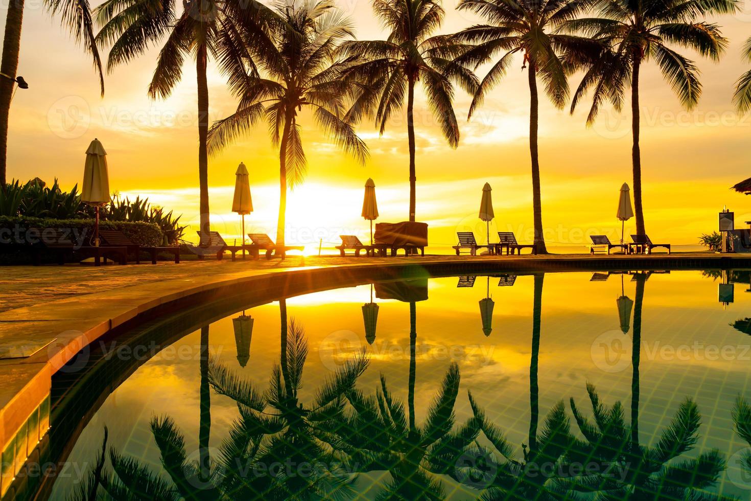 sombrilla y silla alrededor de la piscina en el hotel resort con amanecer en la mañana foto