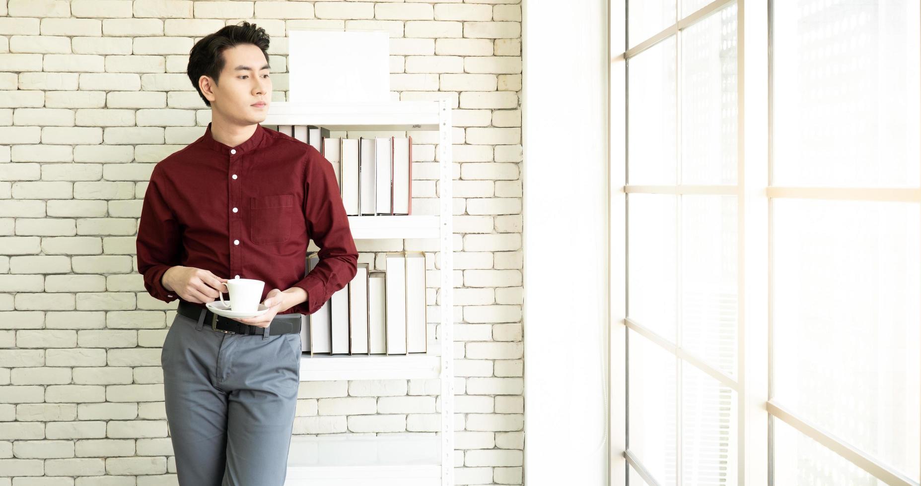 A young handsome asian businessman with confident face standing besides the windows in the working office photo