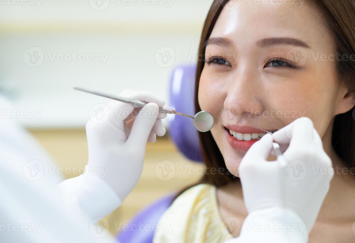 Cierre la imagen del dentista que realiza el cuidado dental y compruebe si hay transportes dentales a la joven asiática en la clínica. concepto de salud y salud dental foto