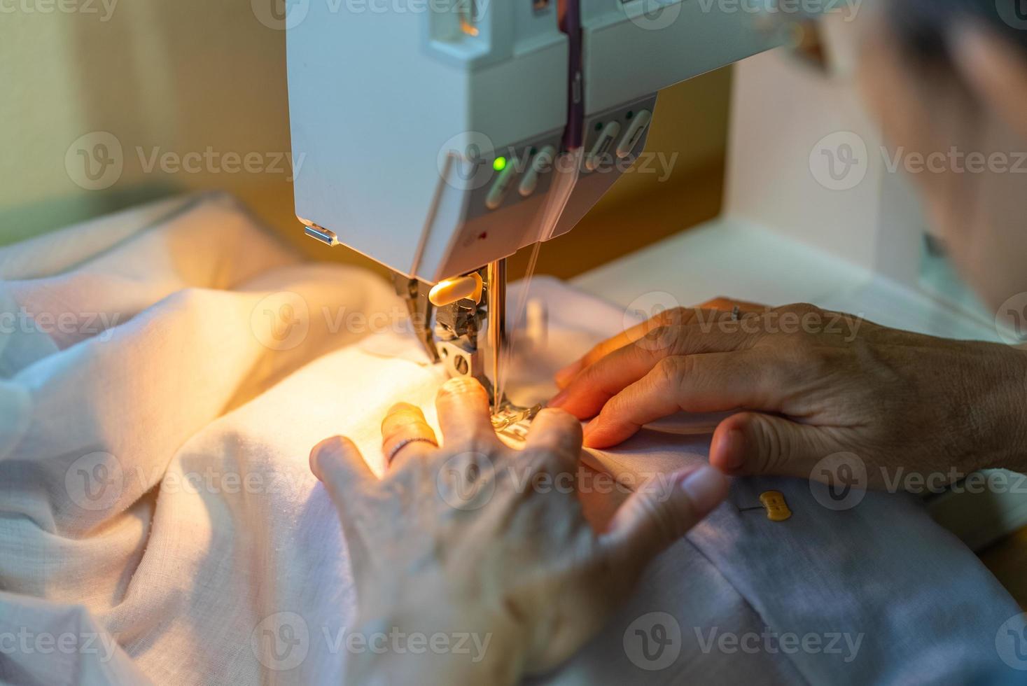 Cerrar las manos de la mujer mayor con máquina de coser para coser ropa en casa foto