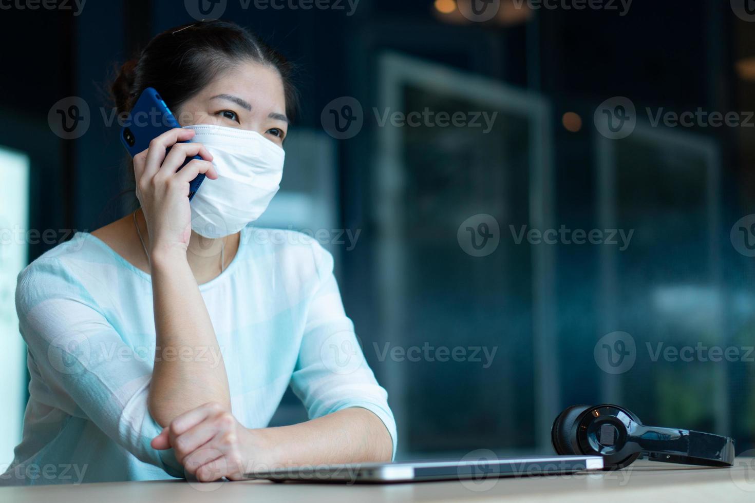Retrato de una joven asiática con mascarilla y auriculares y usando la computadora para trabajar desde casa durante el brote de covid-19 o coronavirus. distanciamiento social y nuevo concepto de estilo de vida normal foto