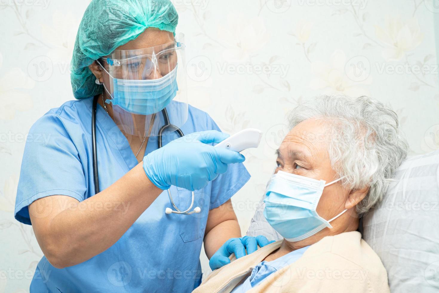 médico asiático con protector facial y traje de ppe nuevo normal para comprobar que el paciente protege la seguridad infección brote de coronavirus covid-19 en la sala de cuarentena del hospital de enfermería. foto