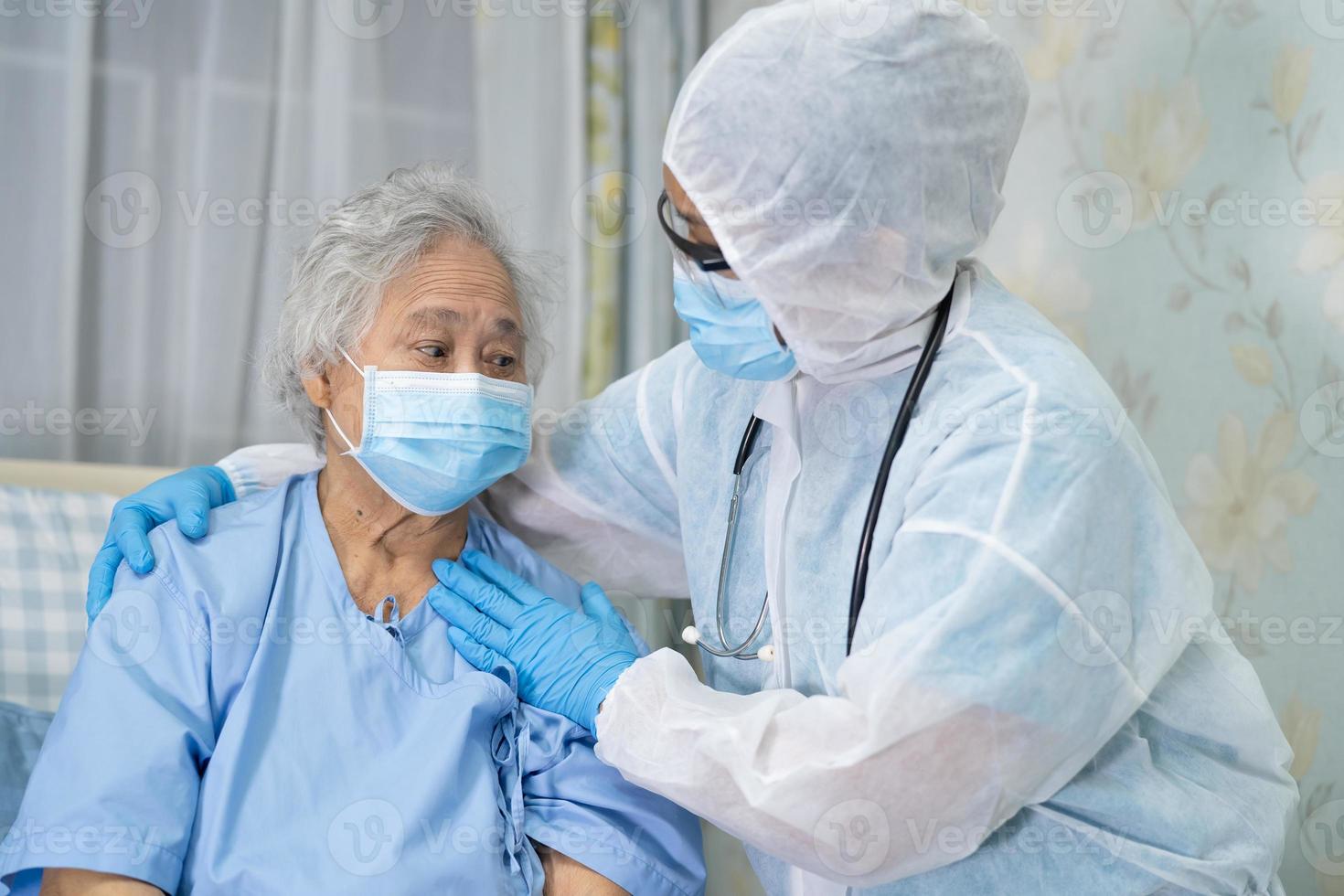 médico asiático con protector facial y traje de ppe nuevo normal para comprobar que el paciente protege la seguridad infección brote de coronavirus covid-19 en la sala de cuarentena del hospital de enfermería. foto