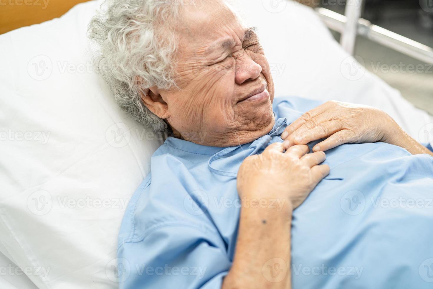 Paciente asiático mayor o anciana mujer siente dolor en el pecho y el corazón en la cama en la sala del hospital de enfermería foto