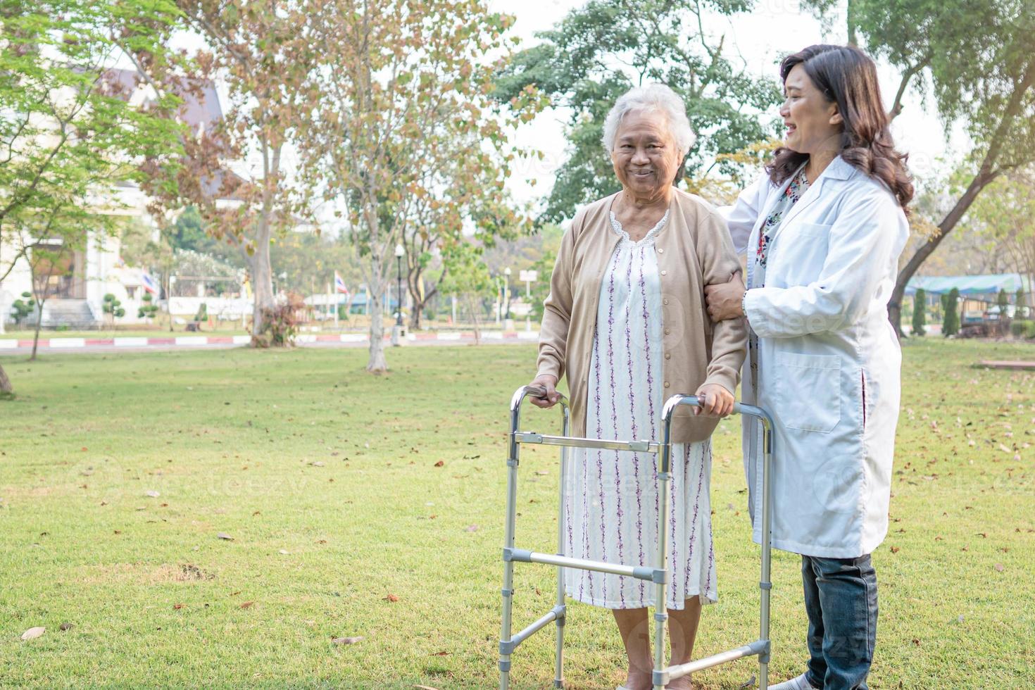 médico ayuda y cuidado anciana asiática anciana o anciana usa andador con una salud fuerte mientras camina en el parque en felices vacaciones frescas. foto