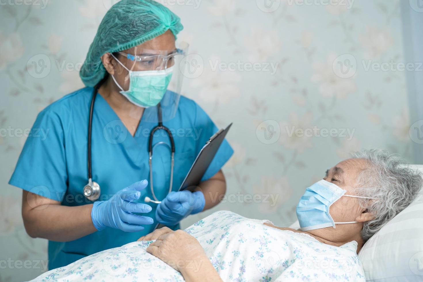 médico asiático con protector facial y traje de ppe nuevo normal para comprobar que el paciente protege la seguridad infección brote de coronavirus covid-19 en la sala de cuarentena del hospital de enfermería. foto