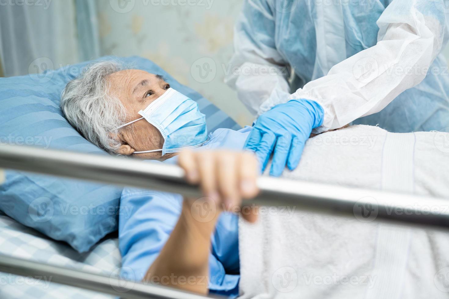 Doctor wearing PPE suit to checking Asian senior or elderly old lady woman patient wearing a face mask in hospital for protect infection Covid-19 Coronavirus. photo