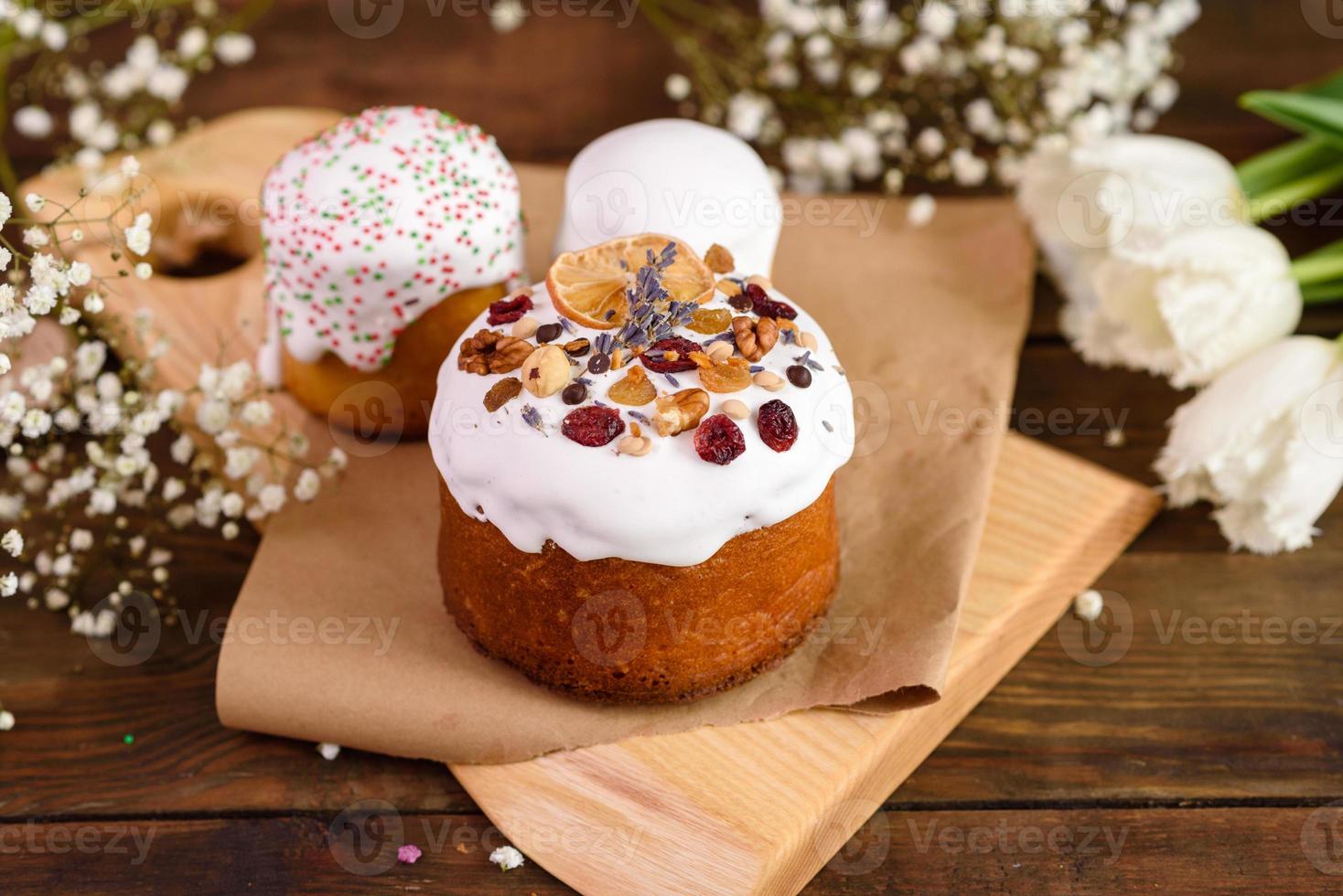 Festive cakes with white glaze, nuts and raisins with Easter eggs on the festive table photo