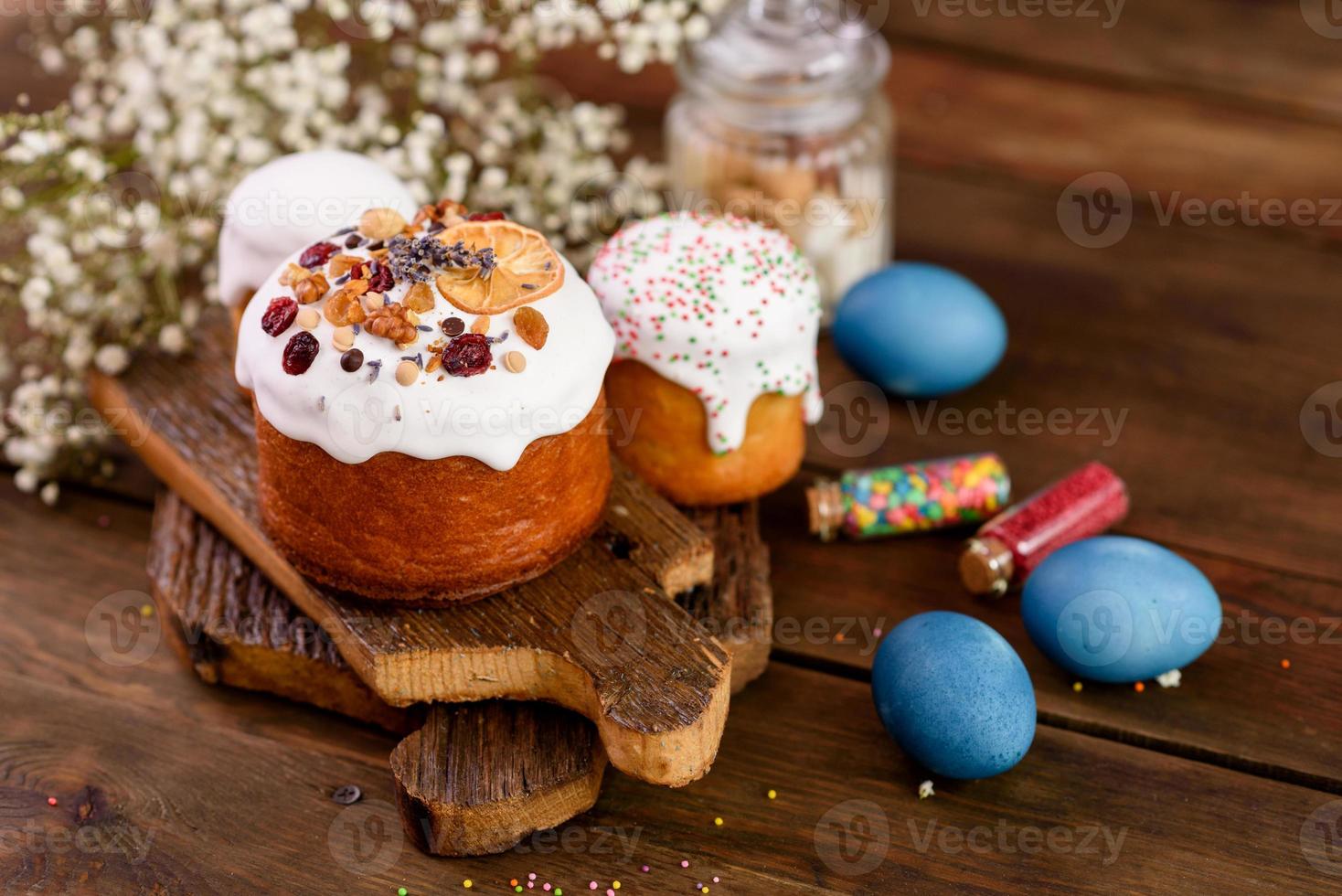 Festive cakes with white glaze, nuts and raisins with Easter eggs on the festive table photo