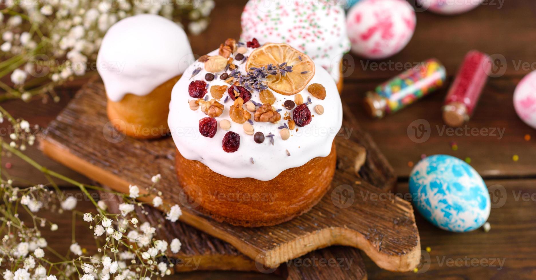 Festive cakes with white glaze, nuts and raisins with Easter eggs on the festive table photo