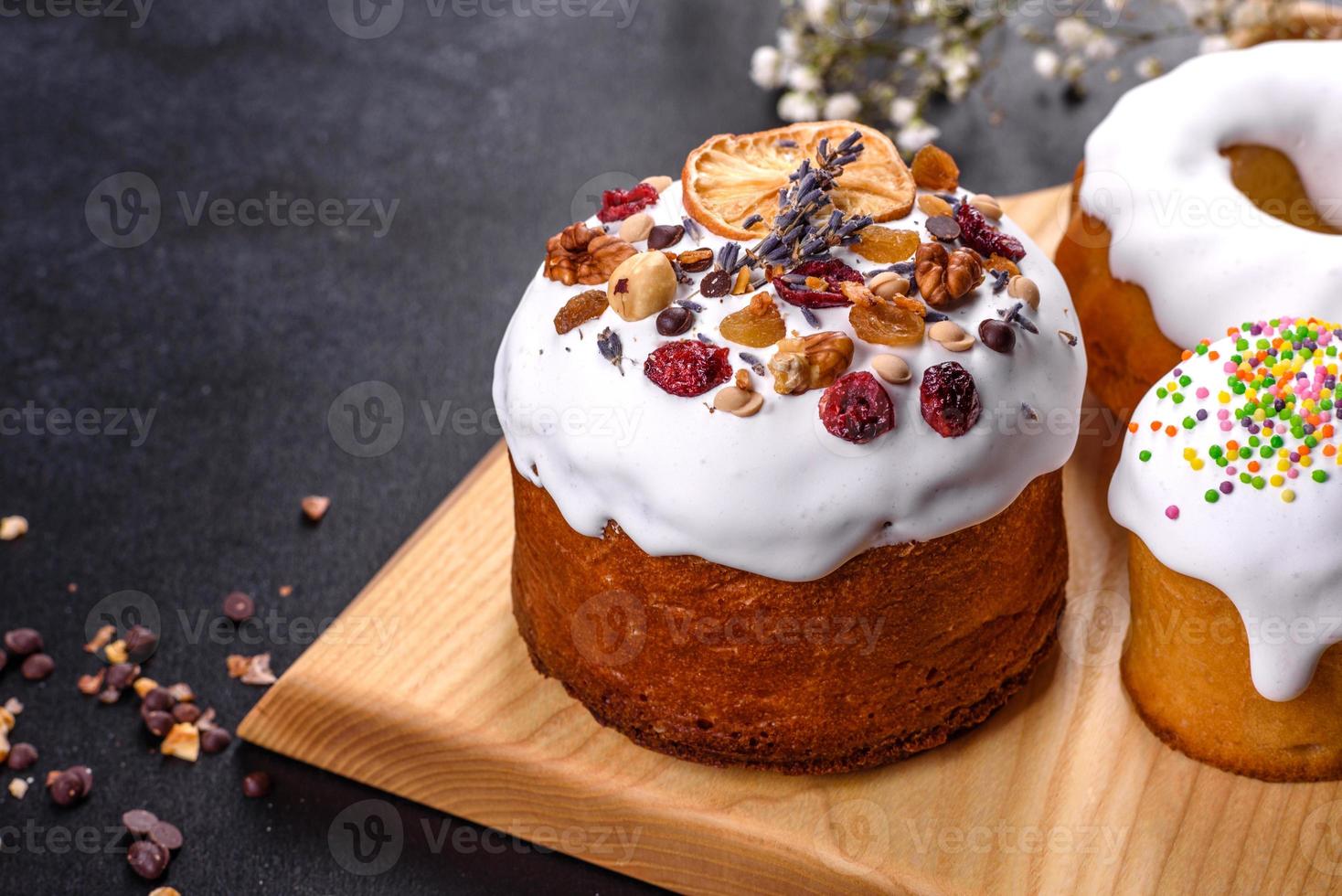 Festive cakes with white glaze, nuts and raisins with Easter eggs on the festive table photo