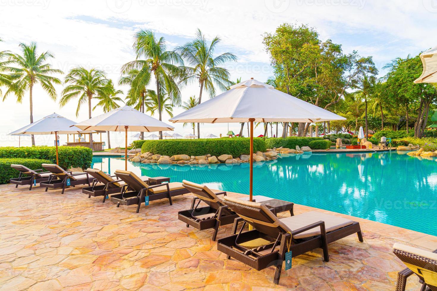 sombrilla y silla alrededor de la piscina en el hotel resort para viajes de placer y vacaciones cerca del mar océano playa foto