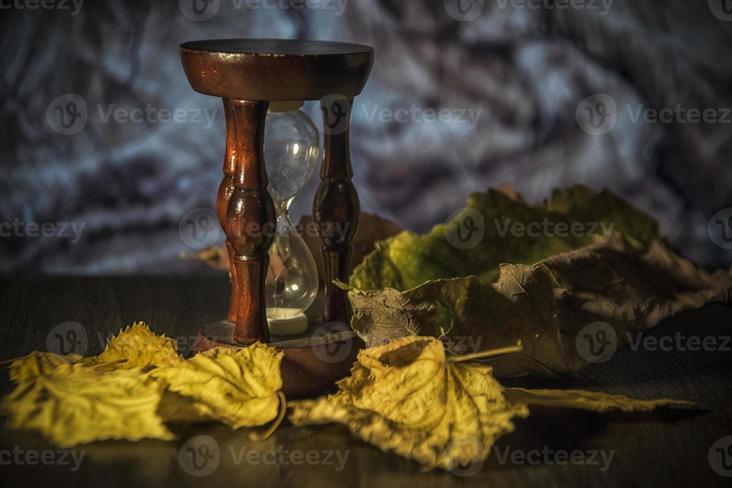 hojas de otoño y un reloj de arena en una mesa foto