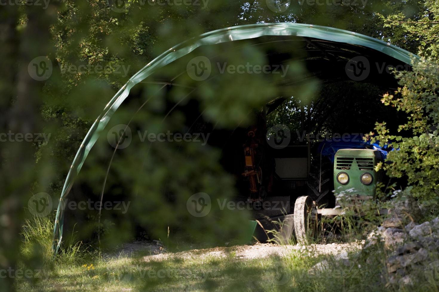 An old tractor hides under the shed in the countryside, France photo