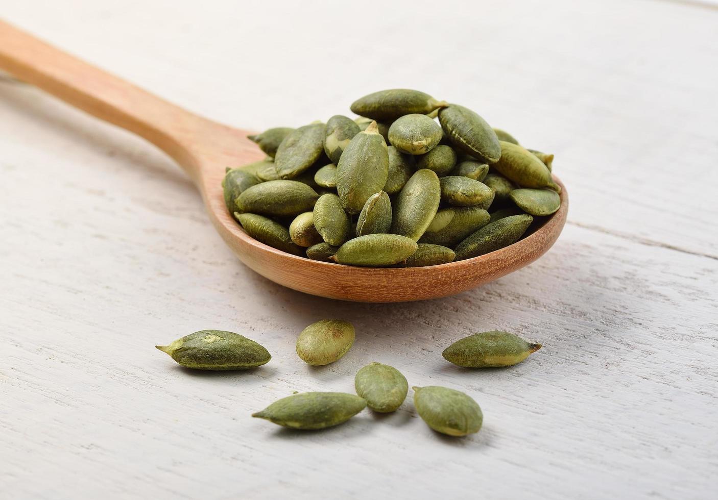 Pumpkin seeds in the spoon on white wooden photo