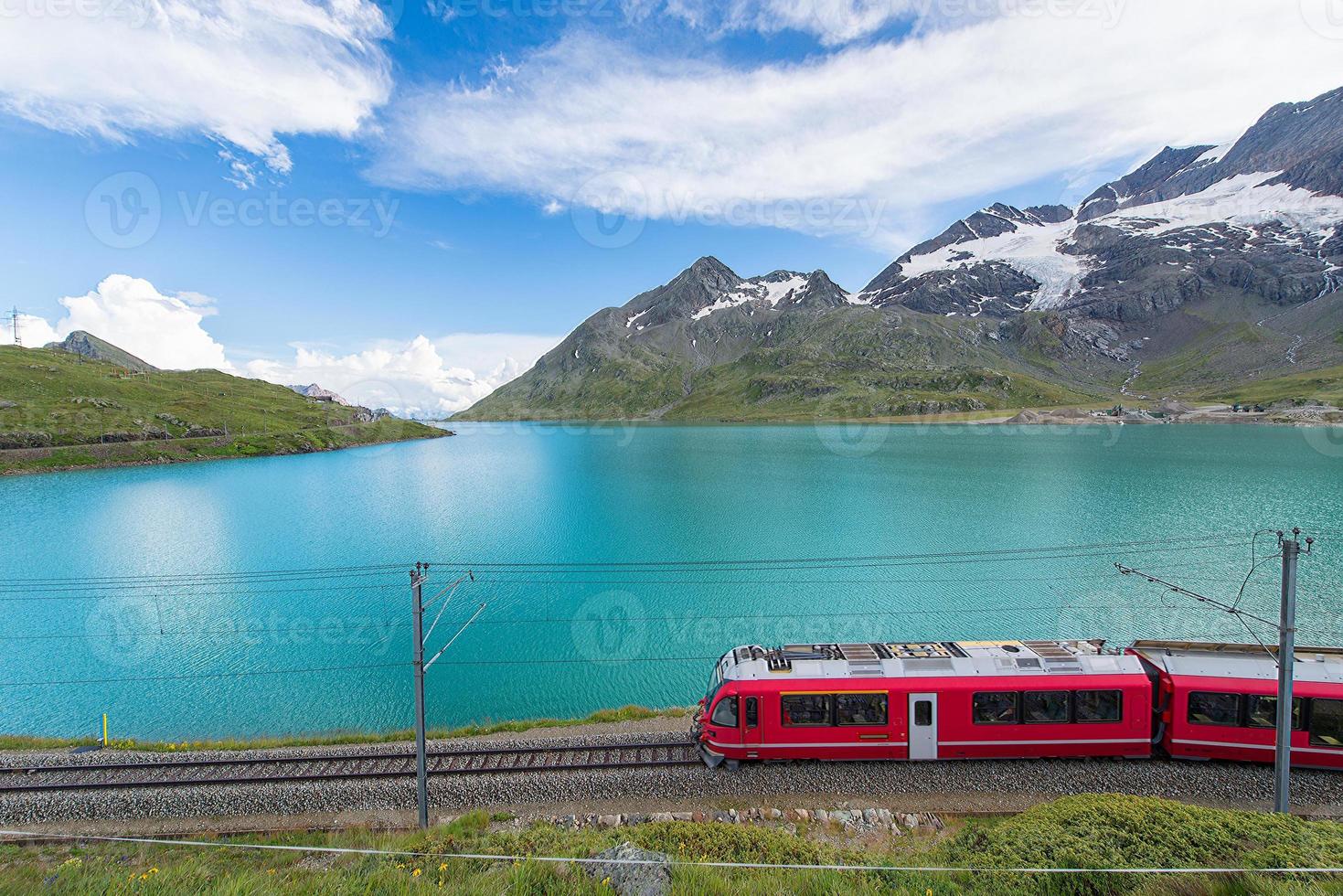 tren rojo en las altas montañas de los alpes suizos pasa cerca de un lago foto