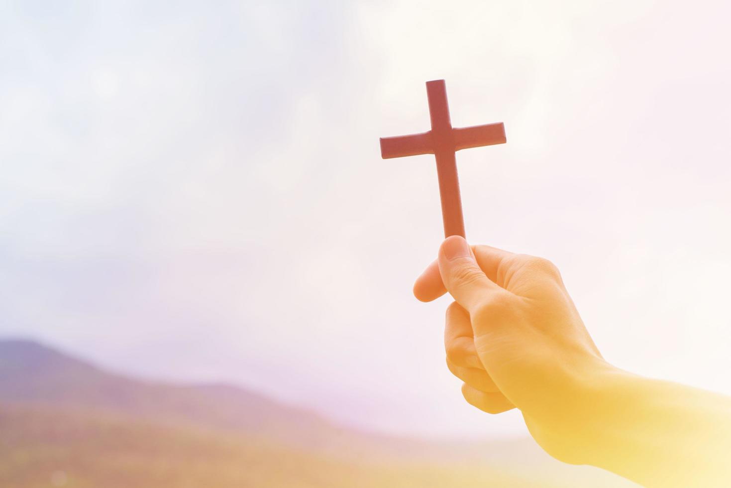 hombre rezando con la cruz, mientras sostiene un símbolo de crucifijo con un rayo de sol brillante en el cielo. foto
