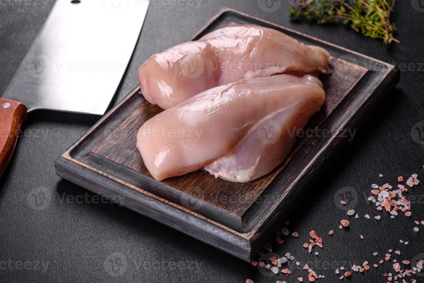 Filete de pollo fresco sobre una mesa de hormigón oscuro con especias y hierbas. foto