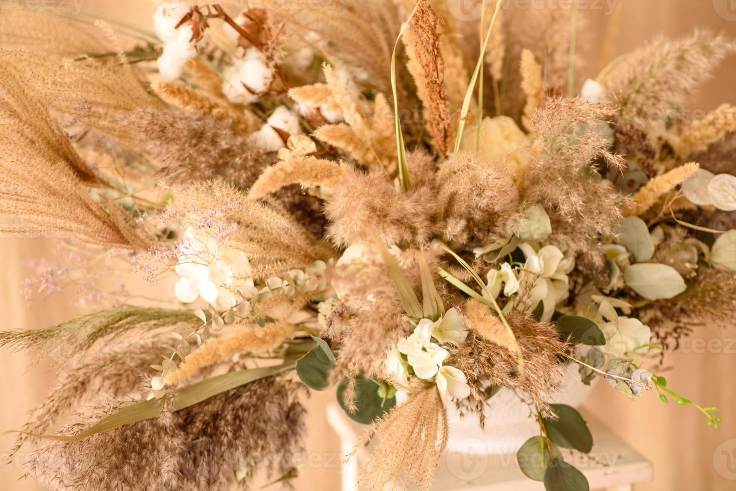 Decorations from dry beautiful flowers in a white vase on a beige fabric background photo
